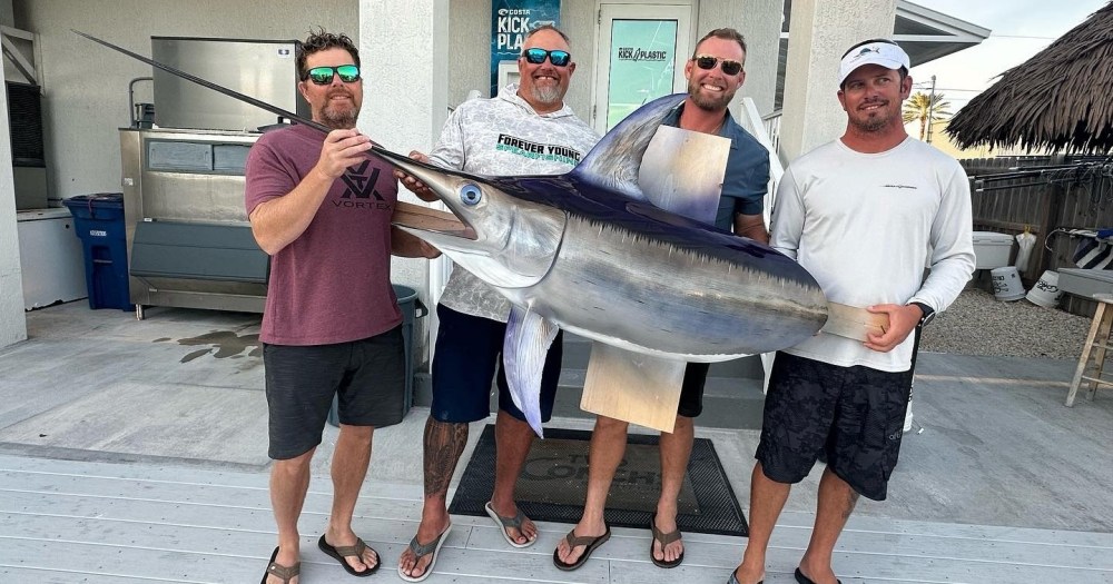 Four men holding a swordfish