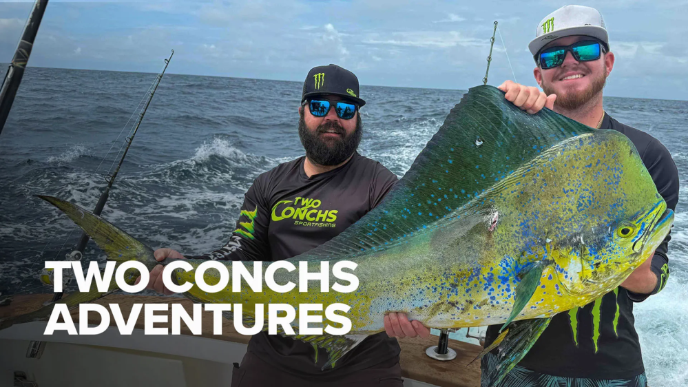 Two men on a boat holding a large fish with 'Two Conchs Adventures' text overlay.