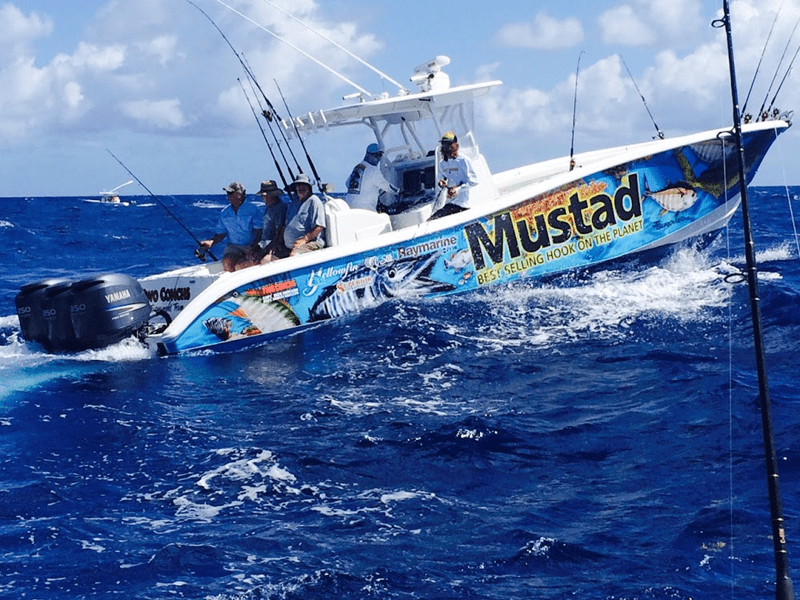 Fishing boat with colorful branding in ocean, carrying six people with fishing rods.
