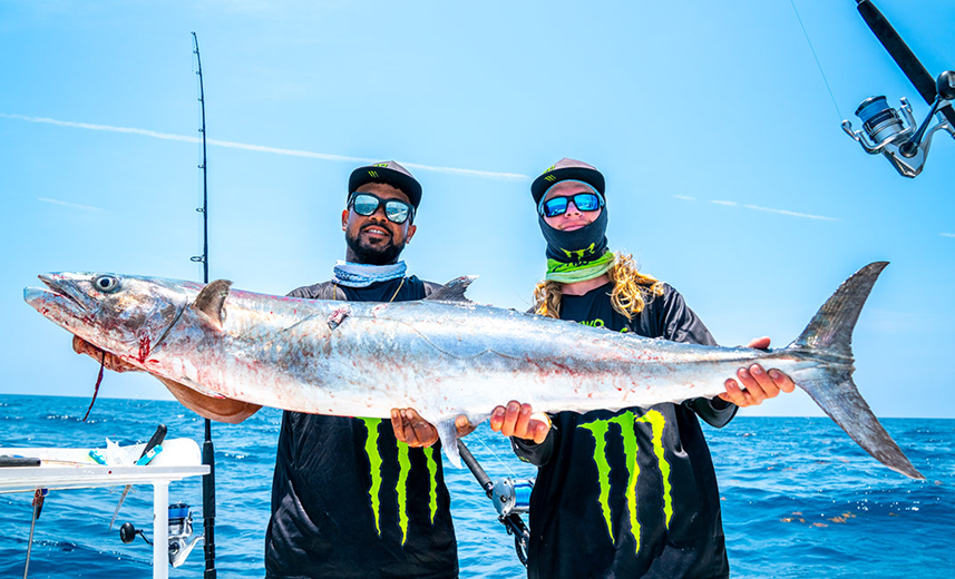 Two people holding a large fish on a boat with a blue sky background.
