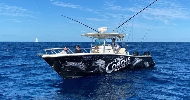 Fishing boat 'Two Conchs' with people onboard on the ocean with another boat in the background.