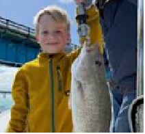 Child in yellow jacket holding a large fish on a boat with a blue sky background.
