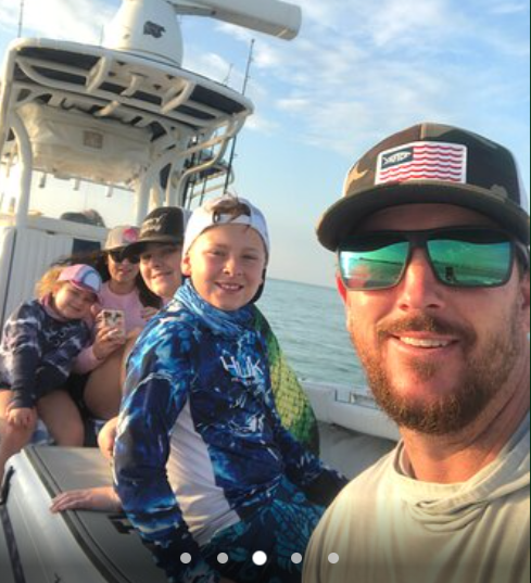 Family on a boat smiling, wearing casual clothes and sunglasses on a sunny day.