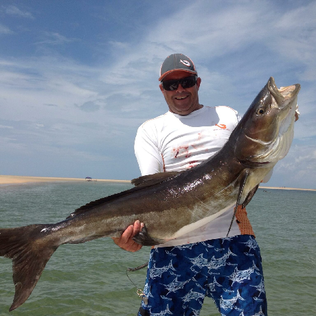 Man holding large fish on a boat under a blue sky.