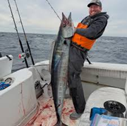 Person on a boat holding a large fish, with fishing rods and ocean in the background.