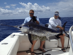 Two men on a boat holding a large swordfish with the ocean in the background.