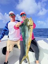Two people on a boat holding a large fish with blue sky and ocean in the background.