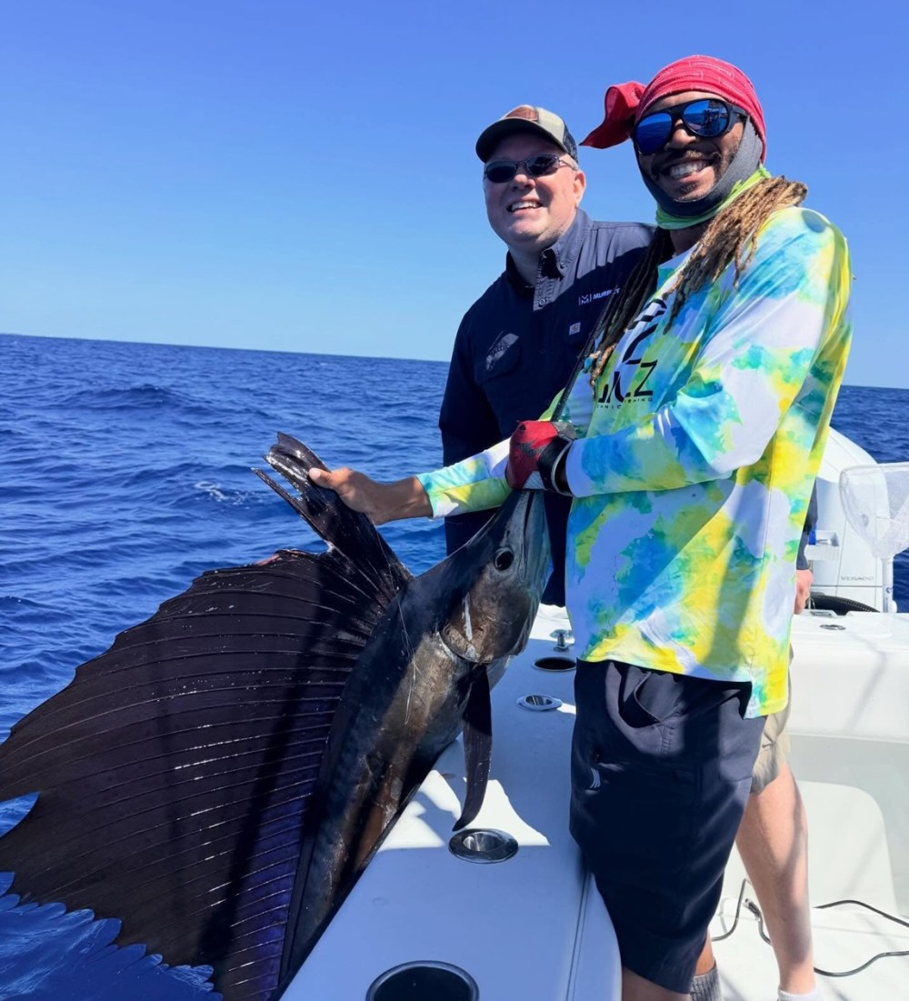 Two men smiling on a boat holding a large sailfish.