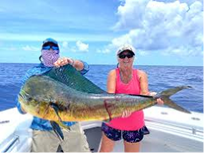 Two people on a boat holding a large fish under a blue sky with clouds.