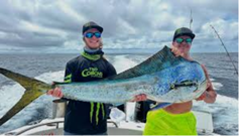 Two people on a boat holding a large fish, ocean in the background.