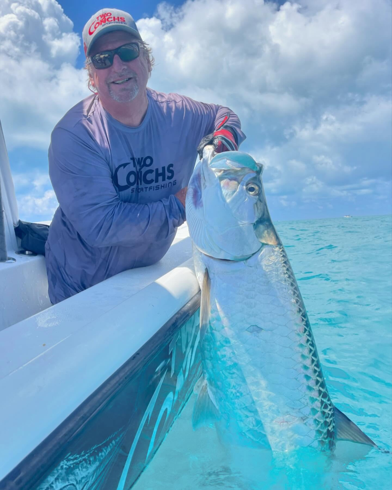 Person on boat holding large fish over clear blue water.