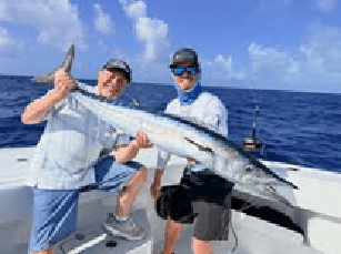 Two people on a boat holding a large fish under a sunny sky.