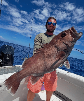 Man holding large Grouper fish on a boat with blue sky and ocean in the background.