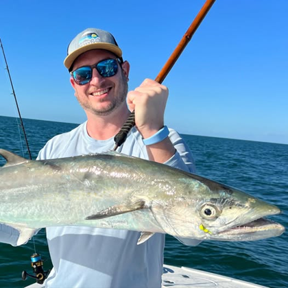 Smiling man in sunglasses holding a kingfish on a boat.