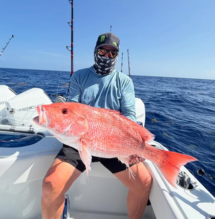 Person on boat holding large red fish, wearing mask and hat.