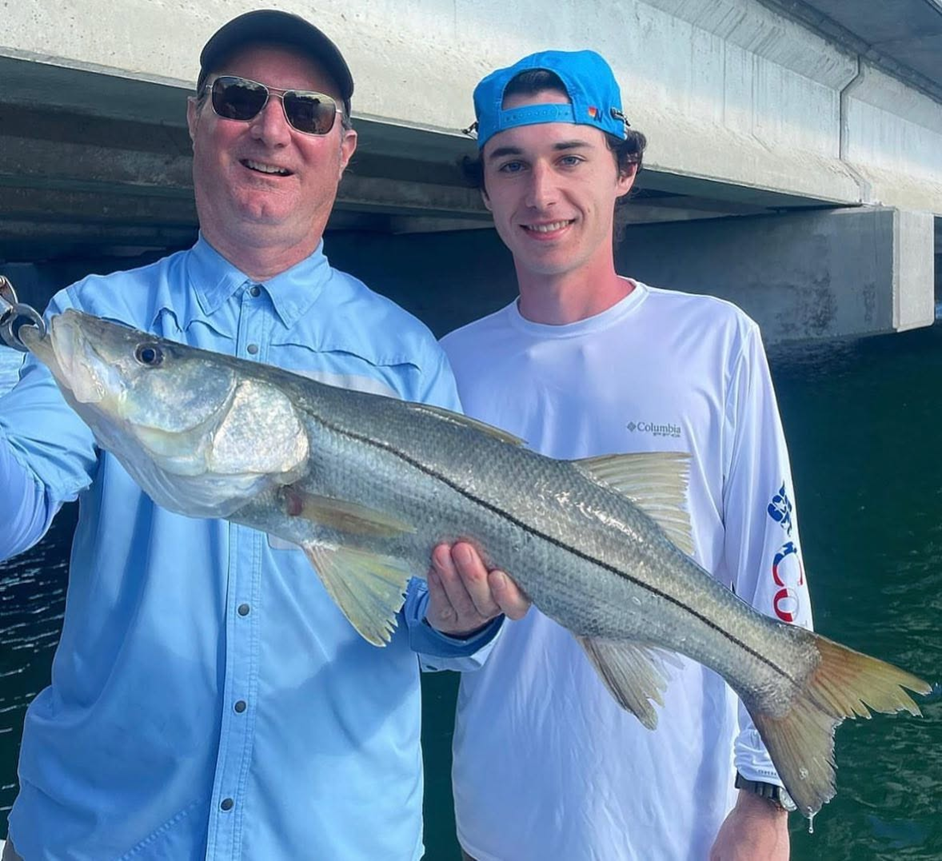 Two people holding a Snook fish under a bridge.