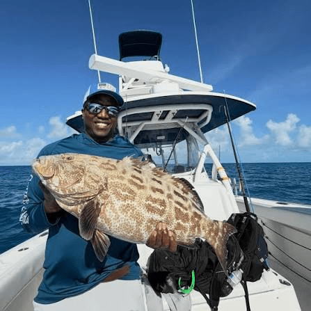 Man on a boat holding a large tilrfish against a sunny ocean backdrop.