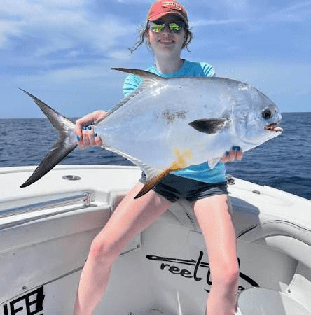 Person sitting on boat holding a large yellow tail snapper fish, ocean in background.