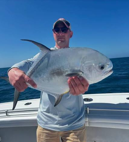 Person holding a yellow tail snapper fish on a boat with ocean background.