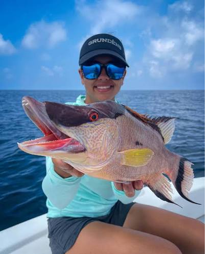 Person holding a large fish on a boat with the sea in the background.