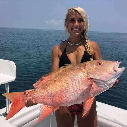 Person holding a large mutton snapper fish on a boat with the ocean in the background.