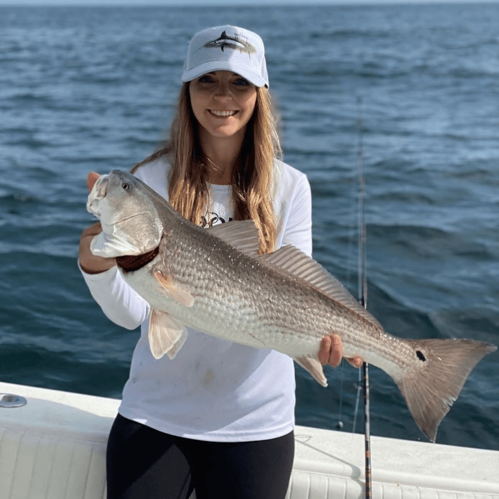 Person in white shirt and cap holding a large redfish on a boat.