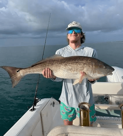 Person holding a large redfish on a boat with ocean in the background.