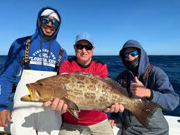Three people holding a large tilefish on a boat, smiling at the camera.