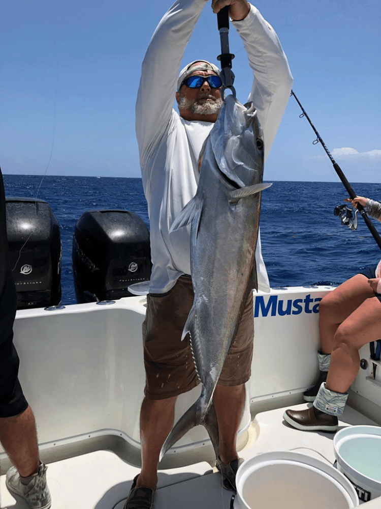 Person holding large Amberjack fish on a boat with ocean in the background.