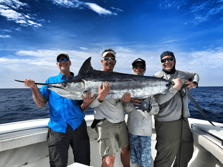 Four people on a Two Conchs Charter holding a large blue marlin under a blue sky.