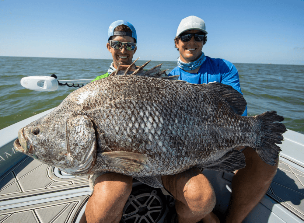 Two people on a Two Conchs Charter boat holding a large Tripletail fish, smiling.